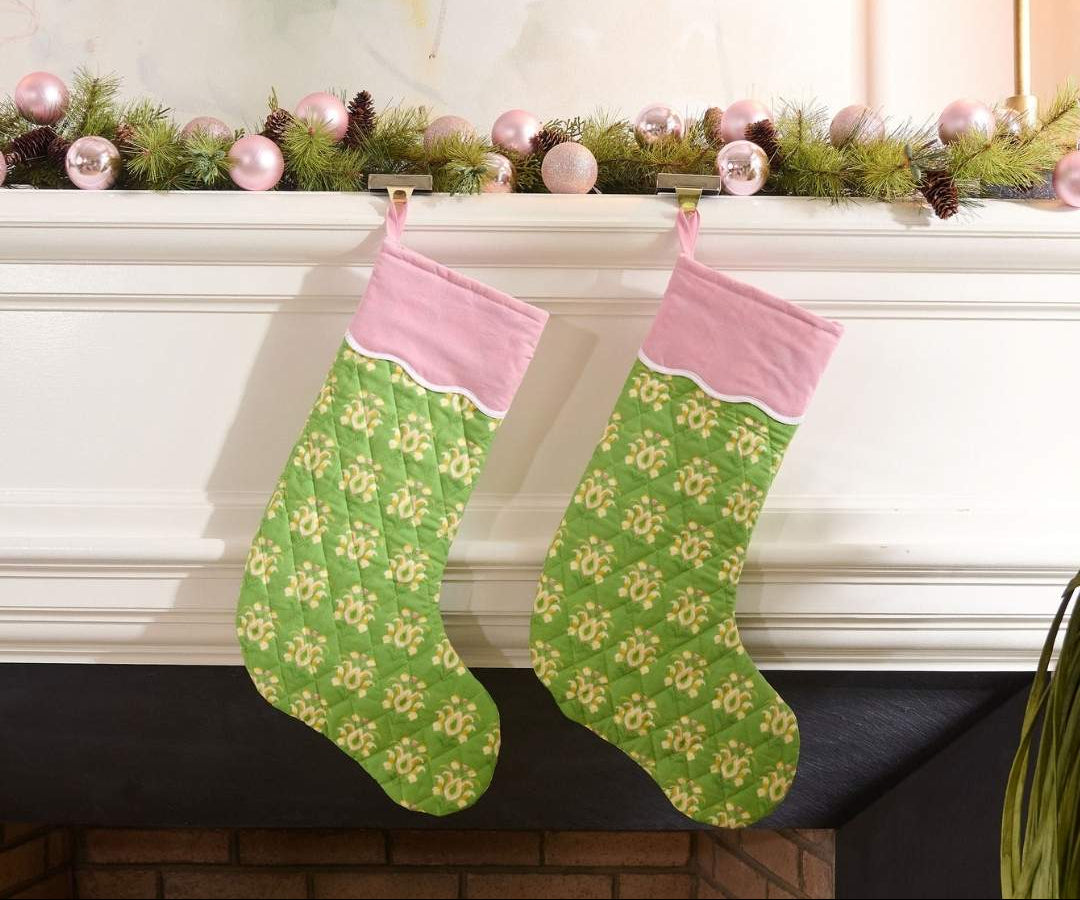Green and pink quilted christmas stocking with a scalloped white detailing, the print is rosemary meadow, a green floral hand painted design by Laura Park hanging on a mantle with holiday garland and pink ornaments. 
